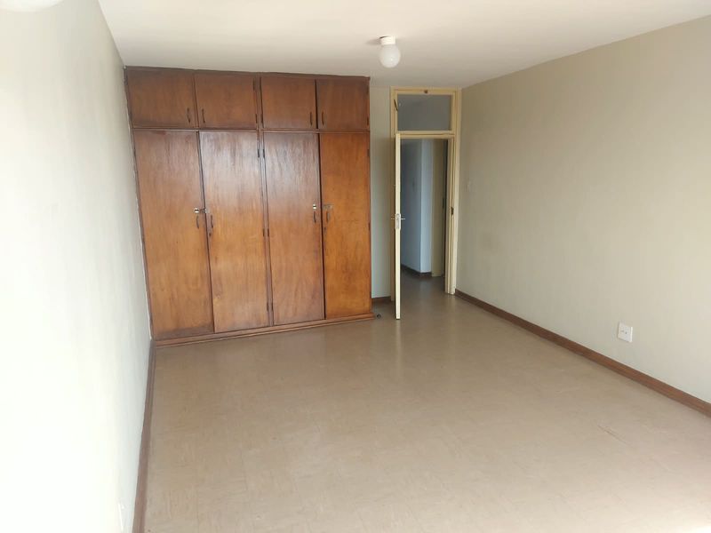 An empty bedroom featuring built-in wooden cupboards with overhead storage and neutral wall finishes, offering a blank canvas for potential updates.