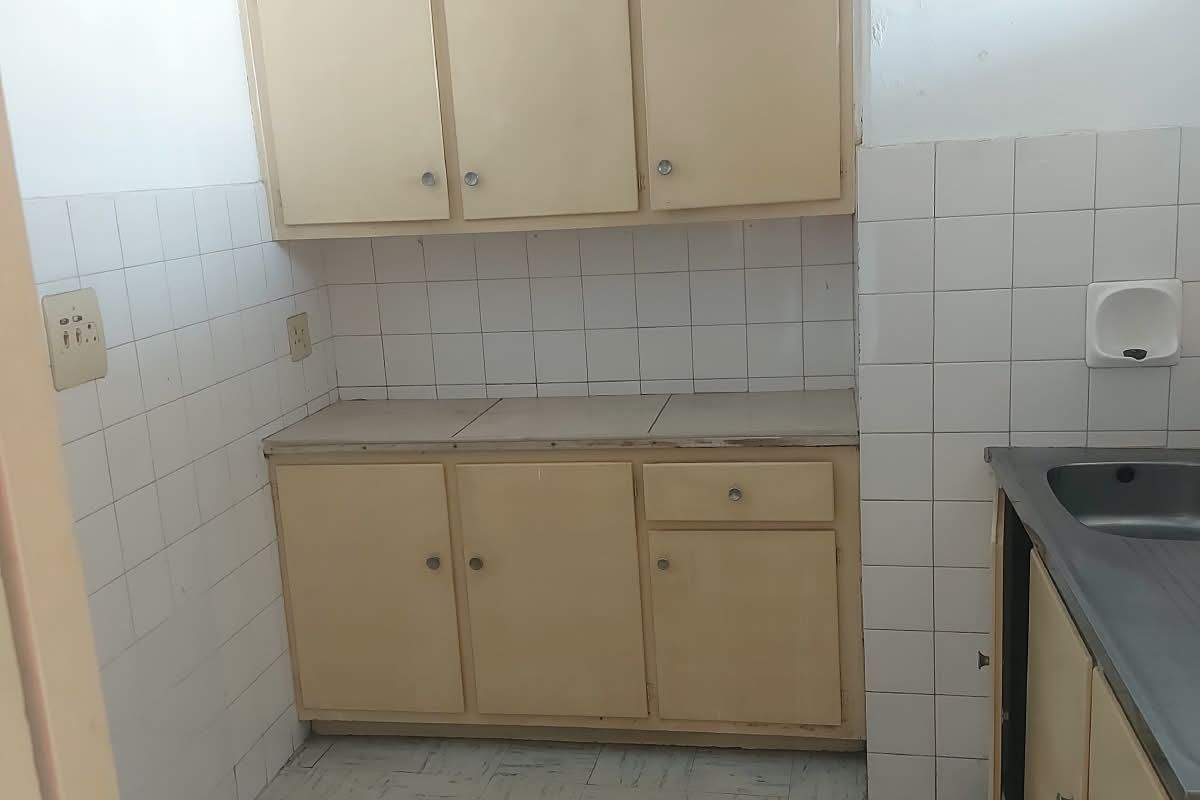 A compact, dated kitchen featuring original built-in cabinetry, tiled splashbacks, and a stainless steel sink, offering significant potential for modernization.
