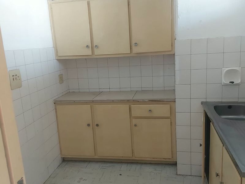 A compact, dated kitchen featuring original built-in cabinetry, tiled splashbacks, and a stainless steel sink, offering significant potential for modernization.