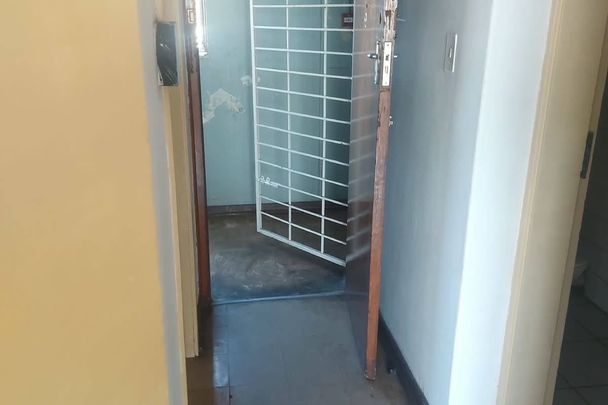 A narrow hallway featuring tiled flooring and a security gate, showing signs of wear and requiring cosmetic updates.