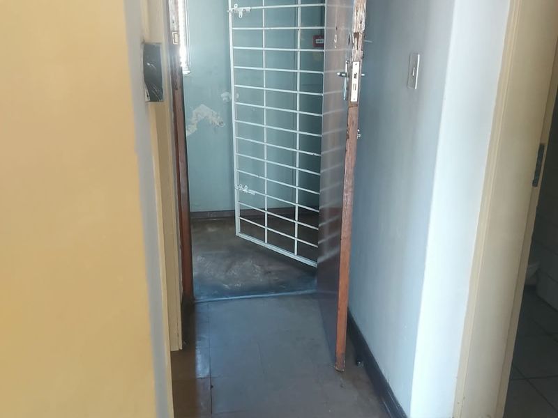 A narrow hallway featuring tiled flooring and a security gate, showing signs of wear and requiring cosmetic updates.