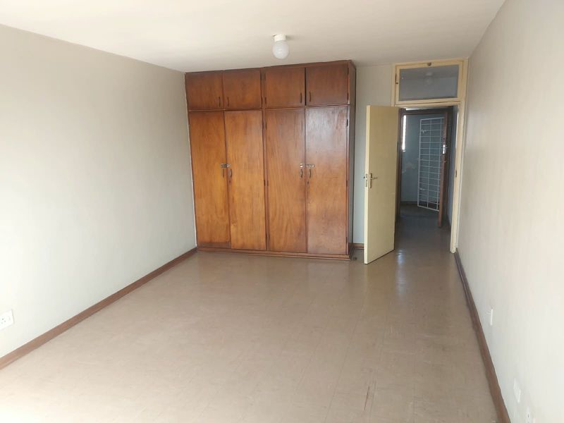 An empty bedroom featuring built-in wooden cupboards, neutral walls, and original flooring, offering a blank canvas for renovation or staging.