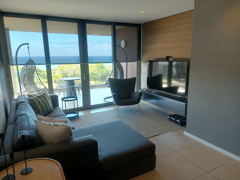 Modern living room featuring timber wall paneling, tiled floors, and large sliding glass doors opening to a balcony with ocean views.