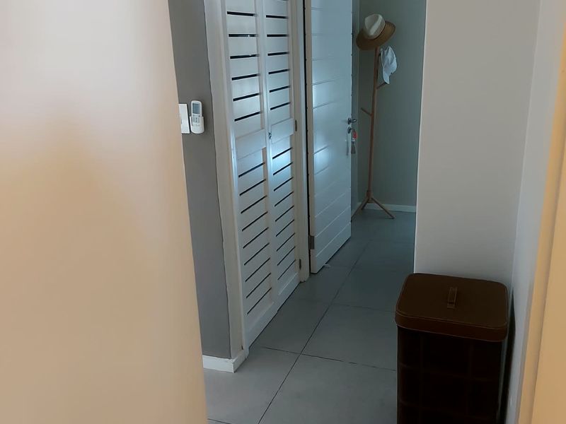 A clean, neutral hallway featuring tiled flooring and white louvered closet doors, providing a bright and functional transition space within the apartment.