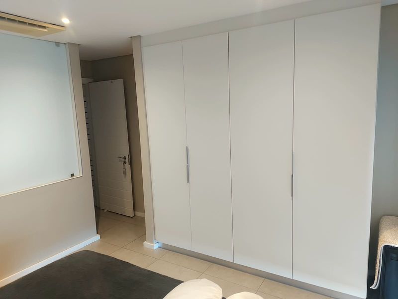 A modern bedroom featuring extensive built-in white cabinetry, sleek tiled flooring, and a contemporary frosted glass partition wall.