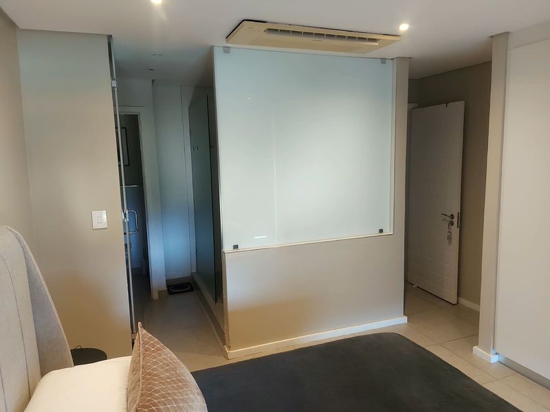 Modern bedroom featuring a sleek frosted glass partition separating the en-suite bathroom, complemented by recessed lighting and integrated ducted air conditioning.