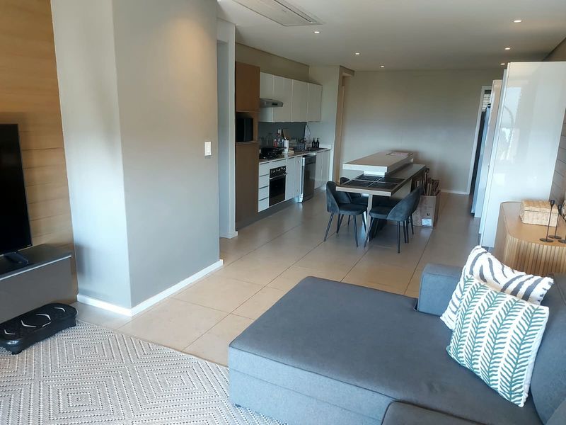 Modern open-plan living area featuring a sleek kitchen with built-in cabinetry, integrated appliances, and tiled flooring throughout, creating a seamless and functional living space.