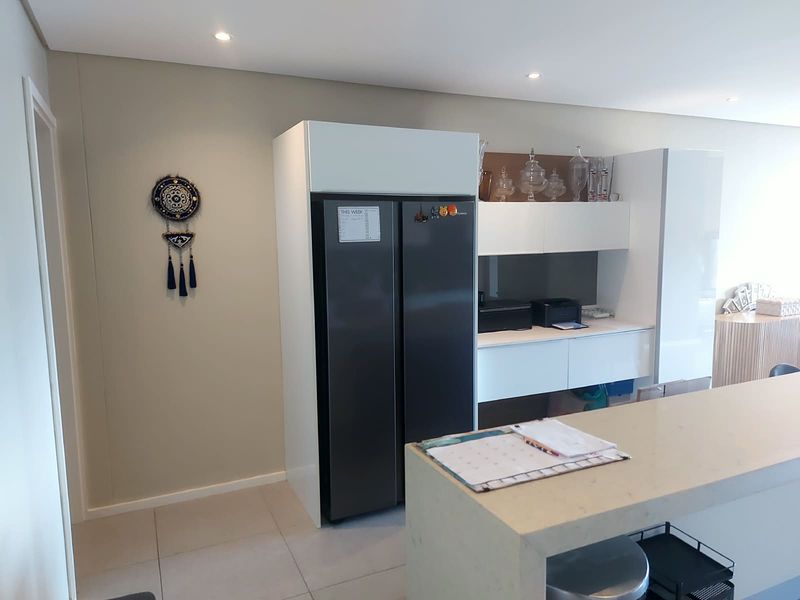 Modern kitchen area featuring sleek white built-in cabinetry, stone countertops, and recessed downlighting, offering a clean and contemporary aesthetic.