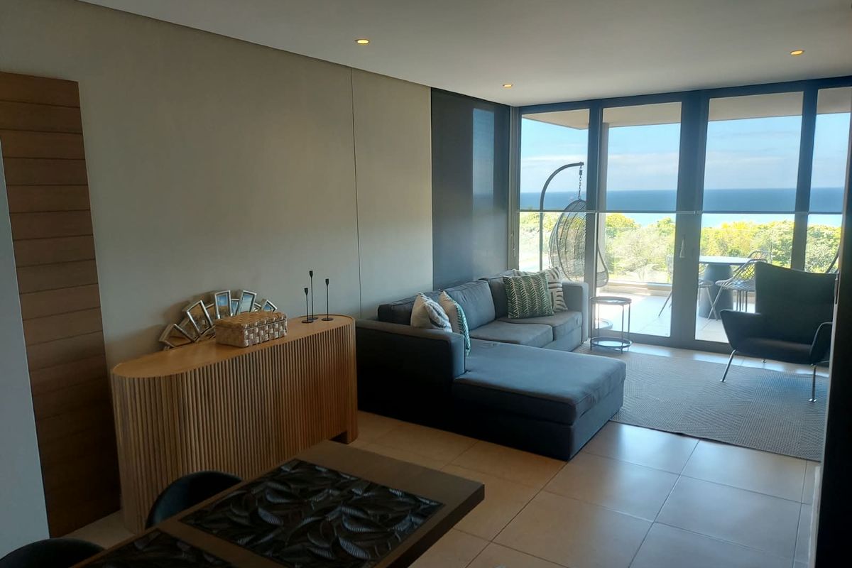 Modern living area featuring tiled floors, recessed lighting, and large sliding glass doors that open onto a balcony with ocean views.