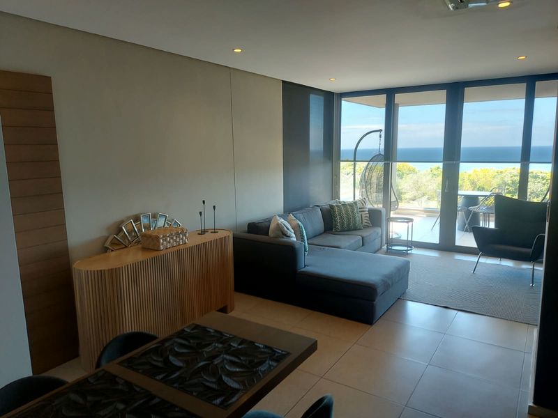 Modern living area featuring tiled floors, recessed lighting, and large sliding glass doors that open onto a balcony with ocean views.