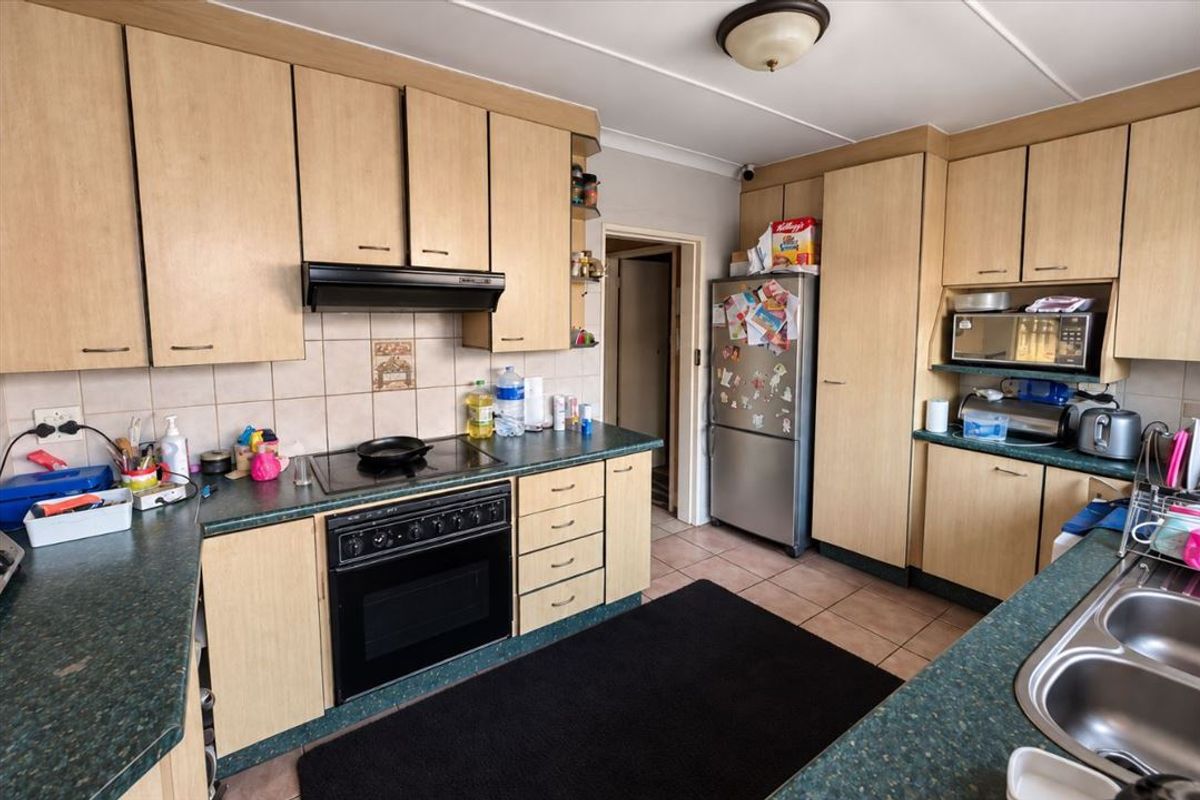 A functional kitchen featuring laminate cabinetry, built-in oven with hob, extractor fan, and double bowl stainless steel sink with tiled backsplash and flooring.