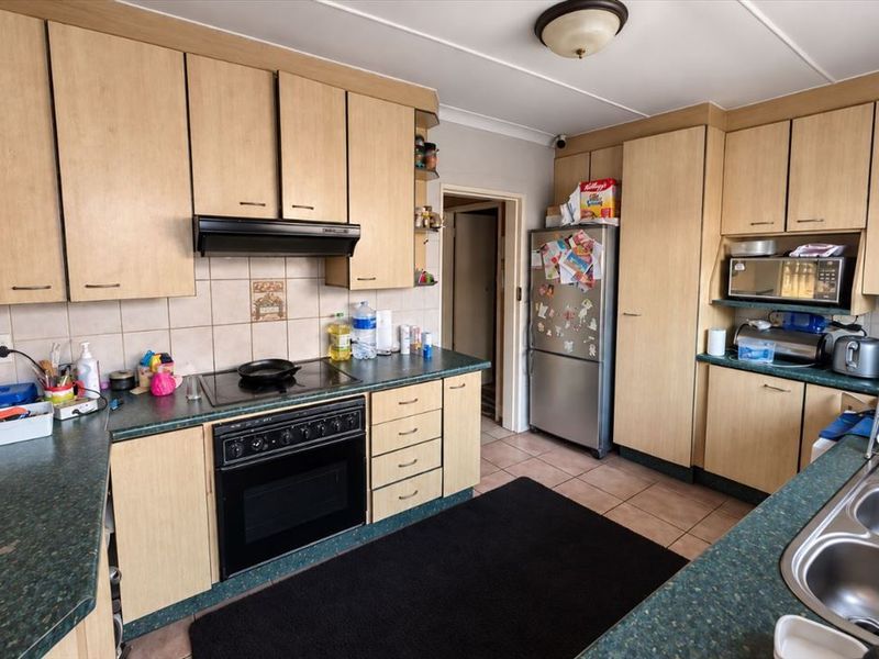 A functional kitchen featuring laminate cabinetry, built-in oven with hob, extractor fan, and double bowl stainless steel sink with tiled backsplash and flooring.