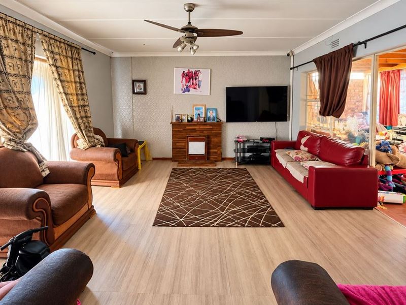 Spacious living room featuring laminate flooring, a ceiling fan, and a built-in fireplace, with direct access to an adjacent enclosed patio area.