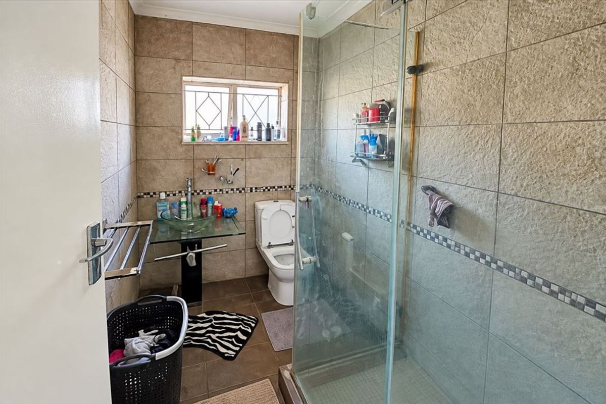 A functional bathroom featuring a glass vessel sink, a toilet, and a glass-enclosed shower with neutral wall and floor tiling.