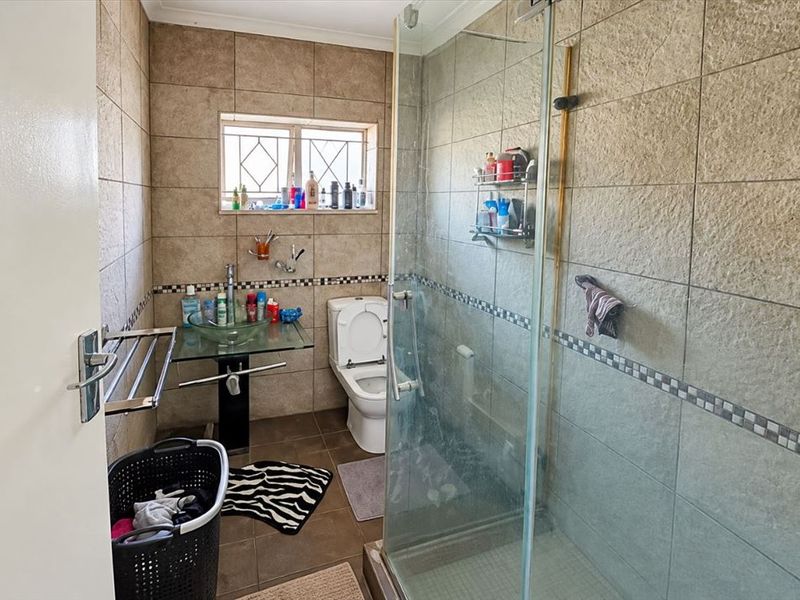 A functional bathroom featuring a glass vessel sink, a toilet, and a glass-enclosed shower with neutral wall and floor tiling.