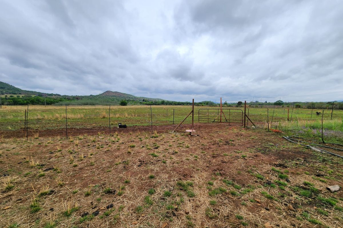 Expansive rural landscape view featuring open grazing land, wire perimeter fencing, and a metal access gate under a cloudy sky.