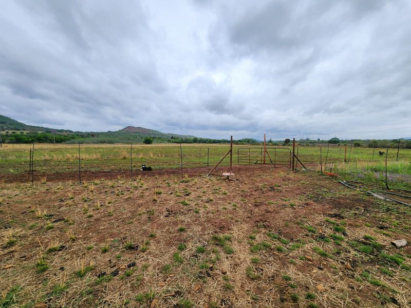 Expansive rural landscape view featuring open grazing land, wire perimeter fencing, and a metal access gate under a cloudy sky.