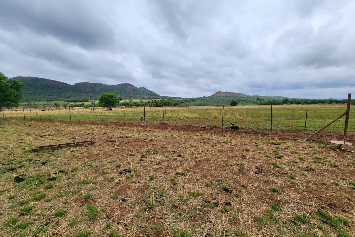 Expansive view of open farm pasture land enclosed by wire fencing with scenic mountain ranges in the background under a cloudy sky.