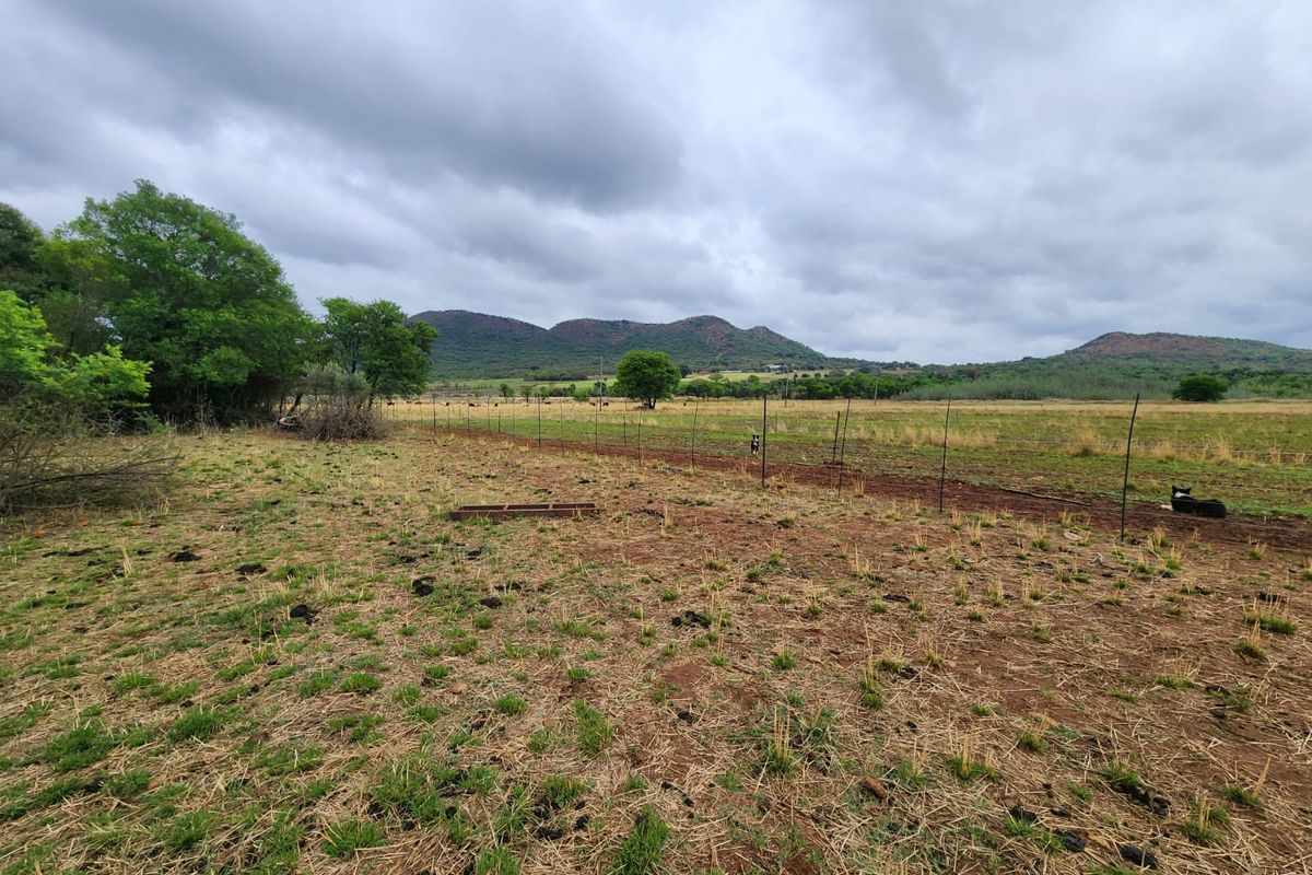 Expansive rural landscape view featuring open pasture land enclosed by wire fencing with distant mountain ranges under a cloudy sky.