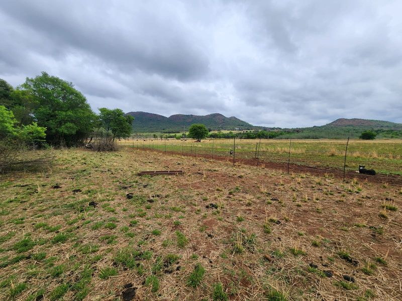 Expansive rural landscape view featuring open pasture land enclosed by wire fencing with distant mountain ranges under a cloudy sky.
