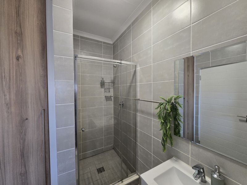 Modern bathroom featuring a glass-enclosed shower, neutral wall tiling, a vanity basin with mixer tap, and built-in storage cabinetry.