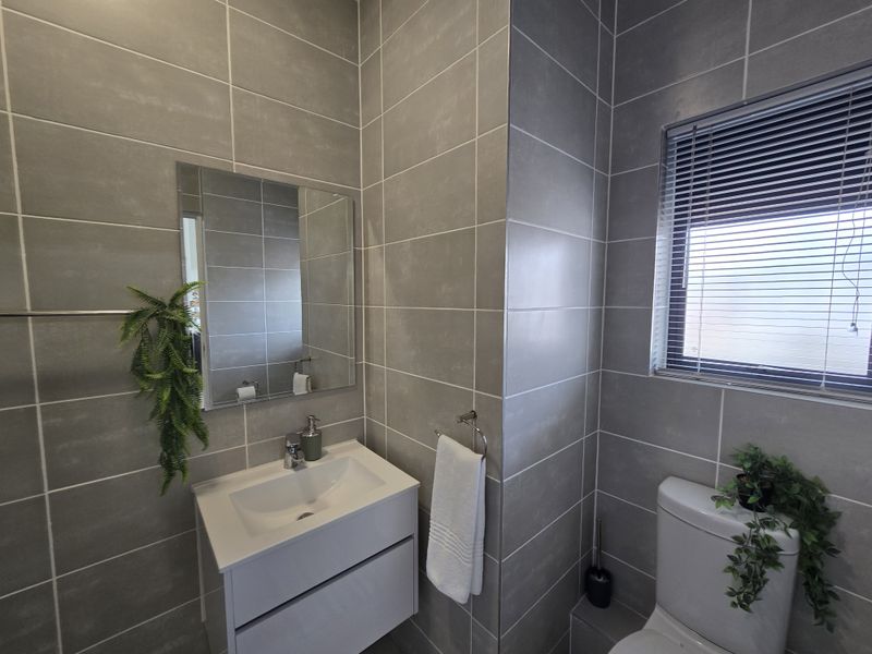 Modern bathroom featuring full-height grey wall tiling, a sleek wall-mounted vanity with basin, and a window with fitted venetian blinds.