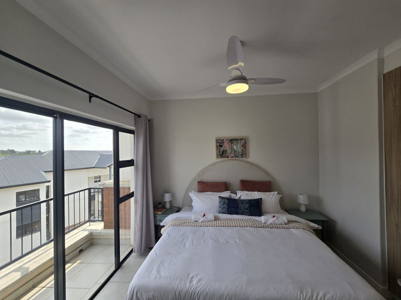 A well-maintained bedroom featuring a ceiling fan, built-in wardrobe, and large sliding glass doors providing direct access to a private balcony.