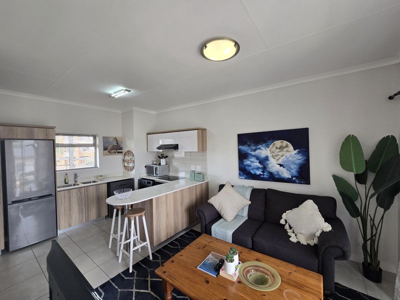 An open-plan living area featuring a modern kitchen with wood-finish cabinetry, a breakfast bar, and tiled flooring, seamlessly connected to the lounge space.