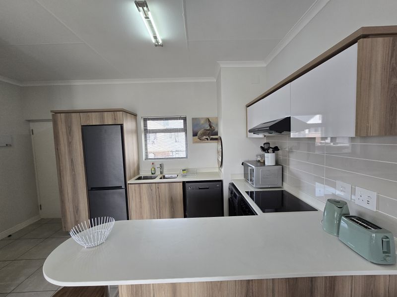 Modern kitchen featuring wood-look cabinetry, white countertops, a breakfast bar, integrated hob, and extractor fan, offering a clean and functional cooking space.