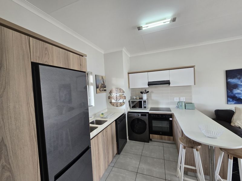 Modern kitchen featuring wood-finish cabinetry, light countertops, integrated appliances, and a convenient breakfast bar, complemented by neutral tiled flooring.