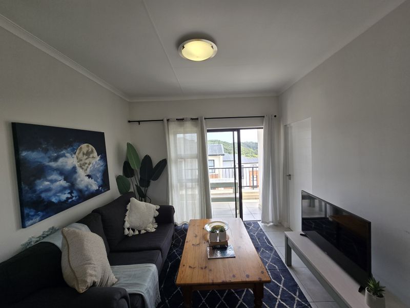 A well-maintained living room featuring tiled flooring, a ceiling light fixture, and a sliding glass door providing access to an outdoor balcony area.