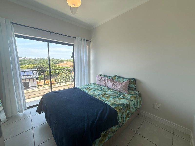 A bedroom featuring tiled flooring, a ceiling fan, and a large sliding glass door that opens onto a balcony with neighborhood views.