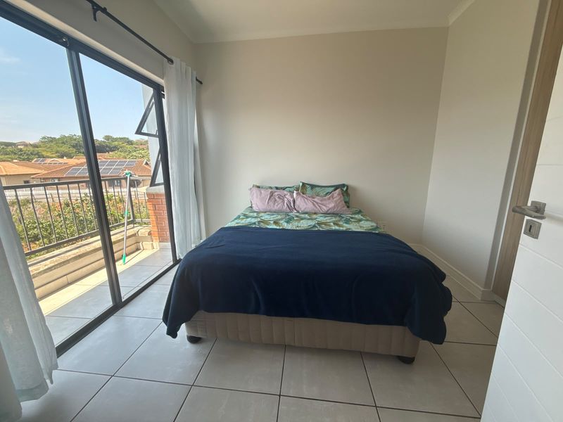 Bright bedroom featuring neutral tiled flooring and large sliding glass doors that provide direct access to a private balcony.
