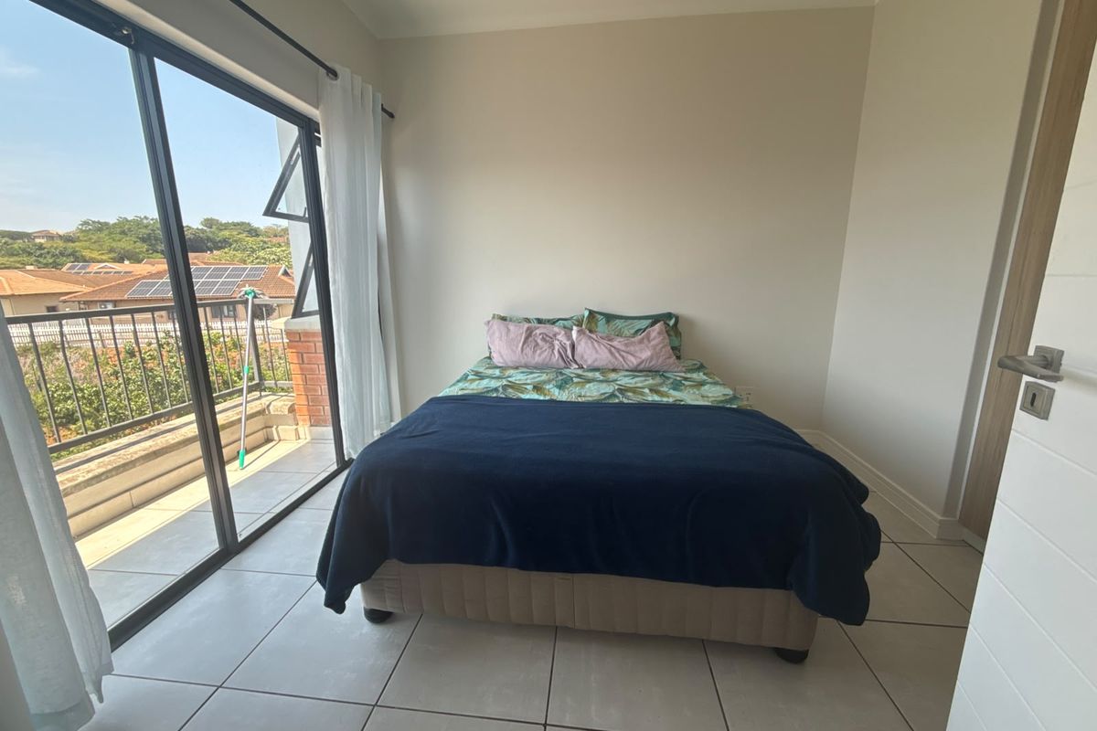 Bright bedroom featuring neutral tiled flooring and large sliding glass doors that provide direct access to a private balcony.