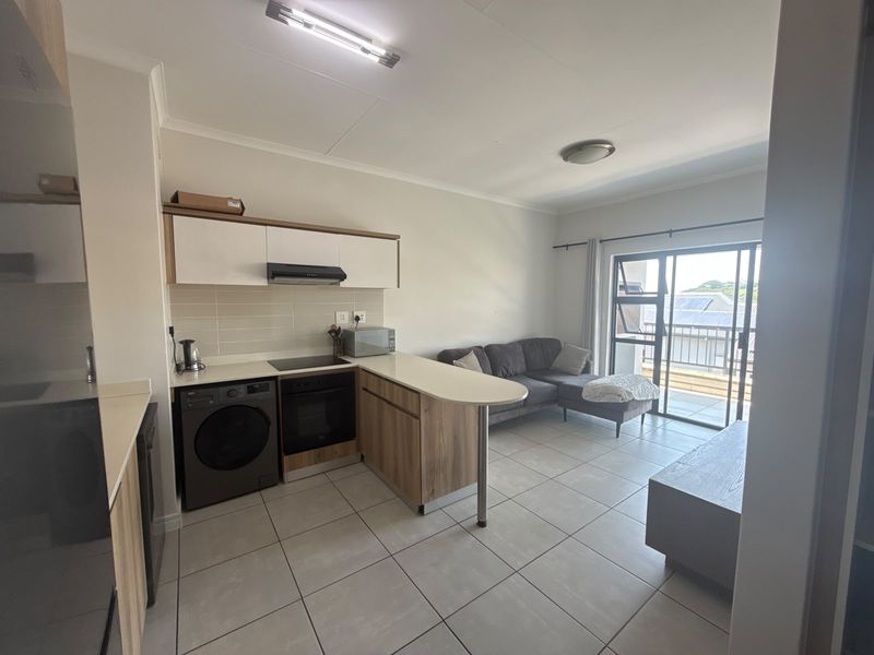 Modern open-plan kitchen and living area featuring tiled floors, built-in cabinetry, integrated appliances, and direct access to a balcony through sliding glass doors.