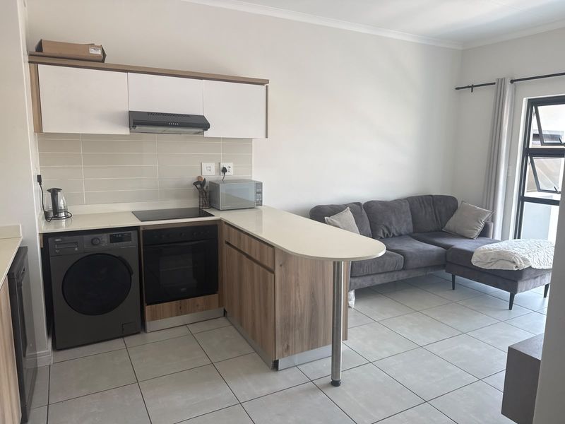 Modern open-plan apartment featuring a compact kitchen with built-in appliances, breakfast bar, and tiled flooring, seamlessly flowing into the living area.