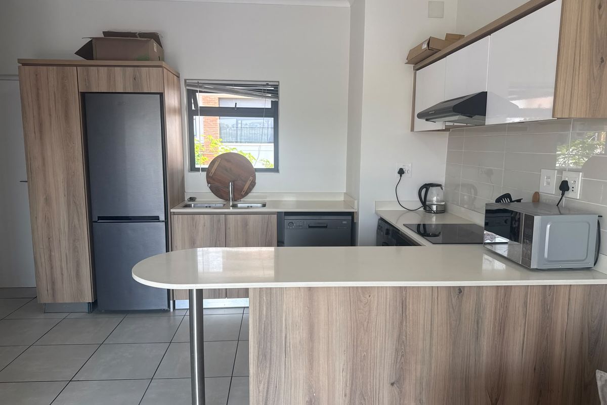 Modern kitchen featuring wood-grain cabinetry, stone countertops, a breakfast bar, and integrated appliances, offering a clean and functional workspace.