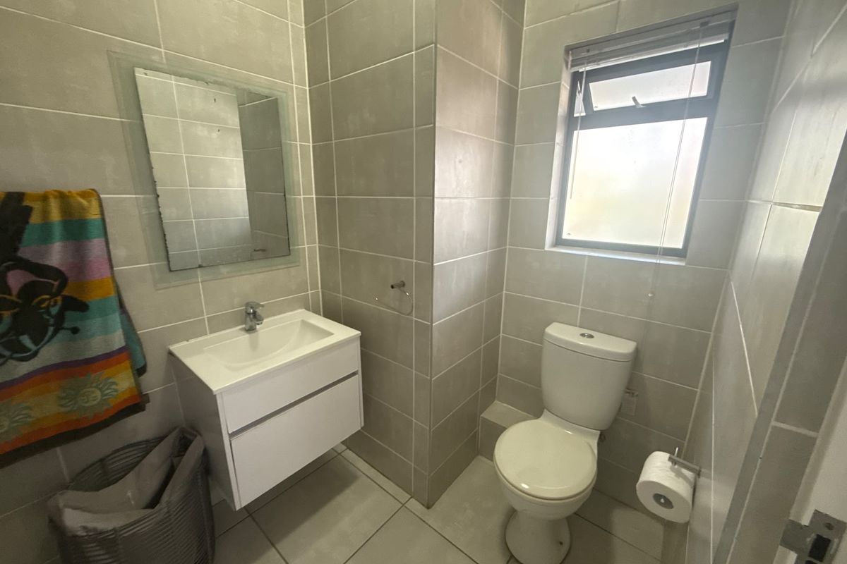 A modern bathroom featuring neutral wall and floor tiles, a wall-mounted vanity with a basin, and a standard toilet.