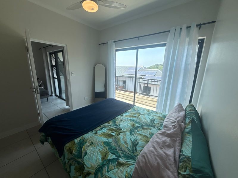A bright bedroom featuring tiled flooring, a ceiling fan, and a sliding glass door that opens onto a balcony with neighborhood views.