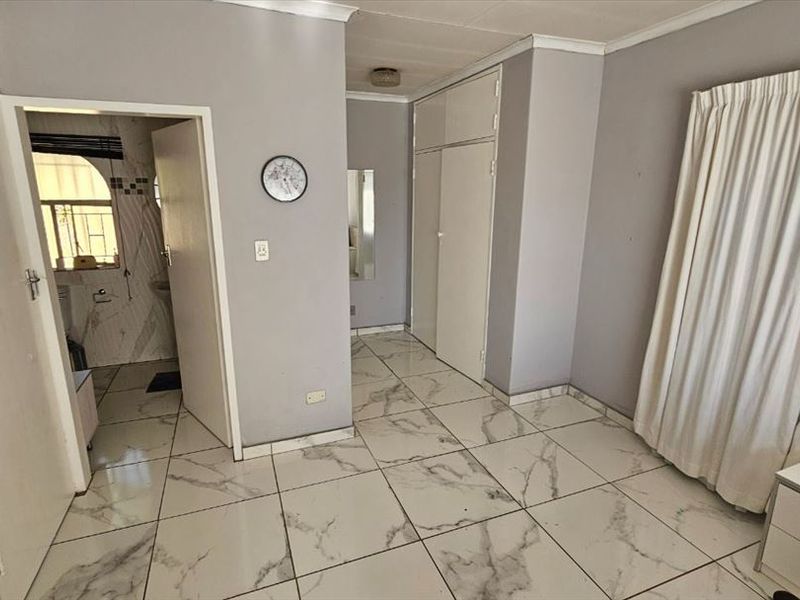 A spacious bedroom featuring modern marble-look tiled flooring and built-in cupboards, offering a clean, neutral canvas ready for personalization.