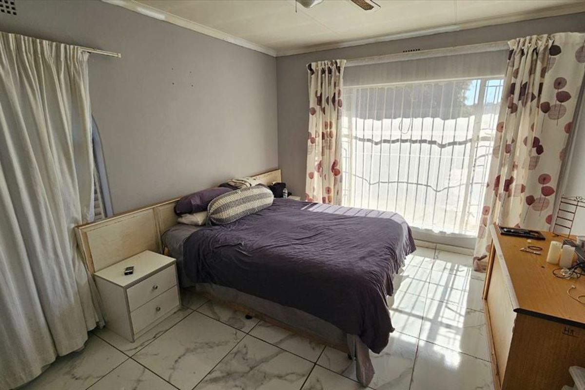 A bedroom featuring tiled flooring, a built-in headboard, and a large window with security gate, offering potential for cosmetic updates.