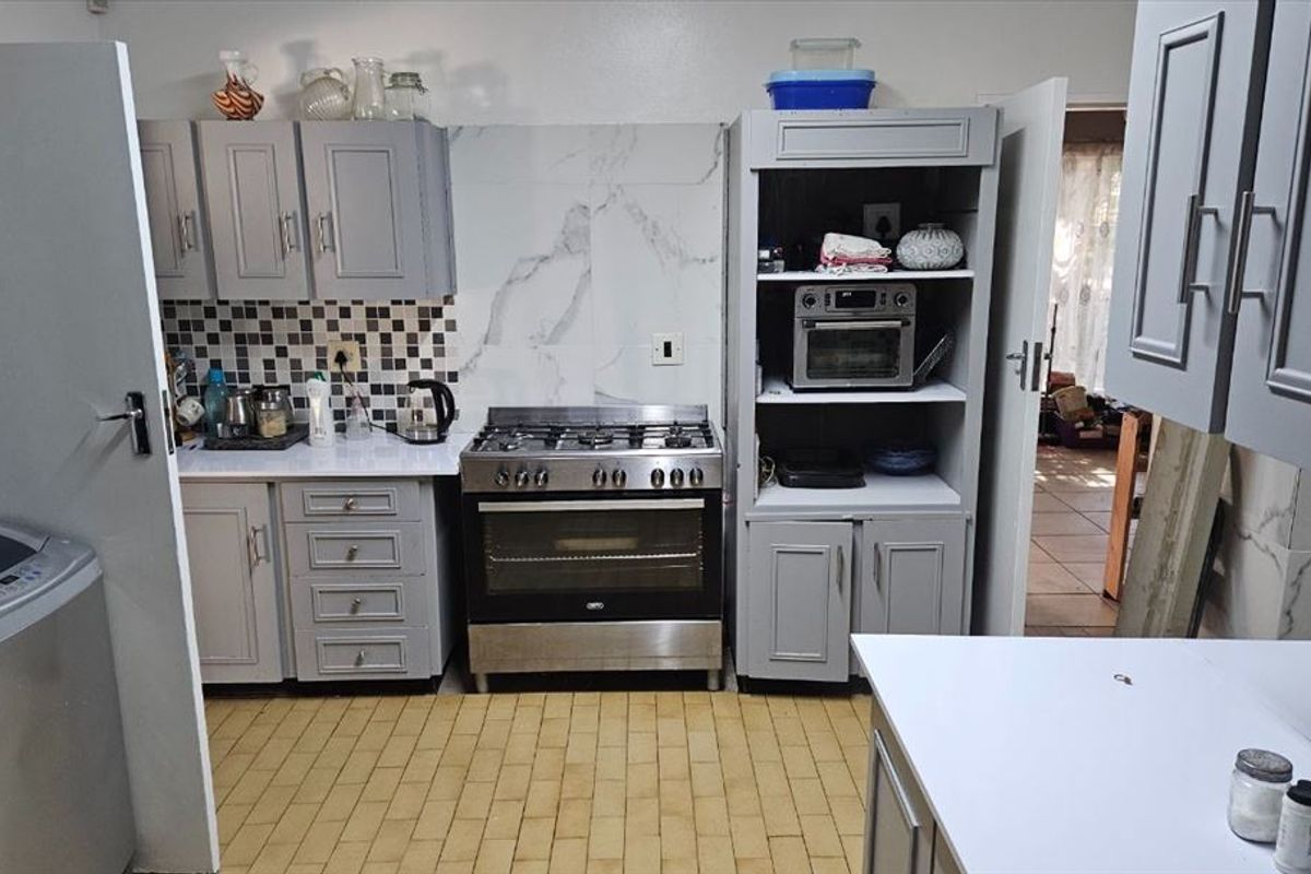A functional kitchen featuring grey cabinetry, a stainless steel gas stove and oven, and a combination of marble-look and mosaic tiled splashbacks.