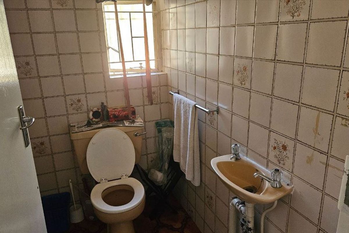 A dated bathroom featuring original ceramic wall tiles, a pedestal basin, and a standard toilet, requiring modernization and renovation of fixed finishes.