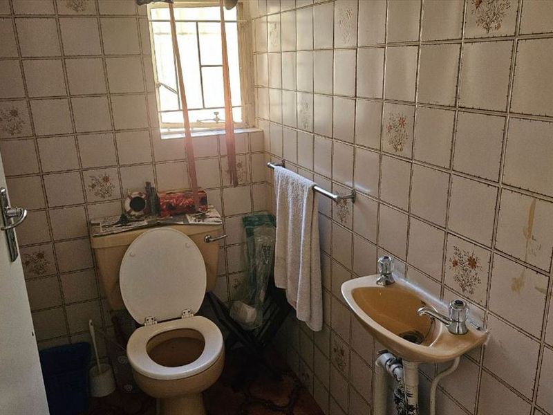 A dated bathroom featuring original ceramic wall tiles, a pedestal basin, and a standard toilet, requiring modernization and renovation of fixed finishes.