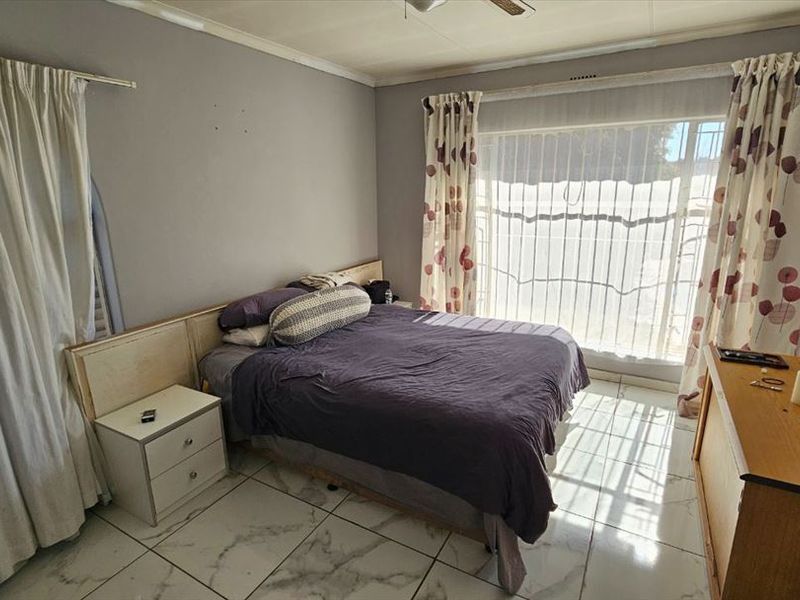 A bedroom featuring tiled flooring, a built-in headboard, and a large window with security gate, offering potential for cosmetic updates.