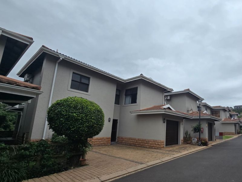 A view of the front facade of a multi-unit residential complex featuring paved driveways, garage access, and neutral exterior finishes.