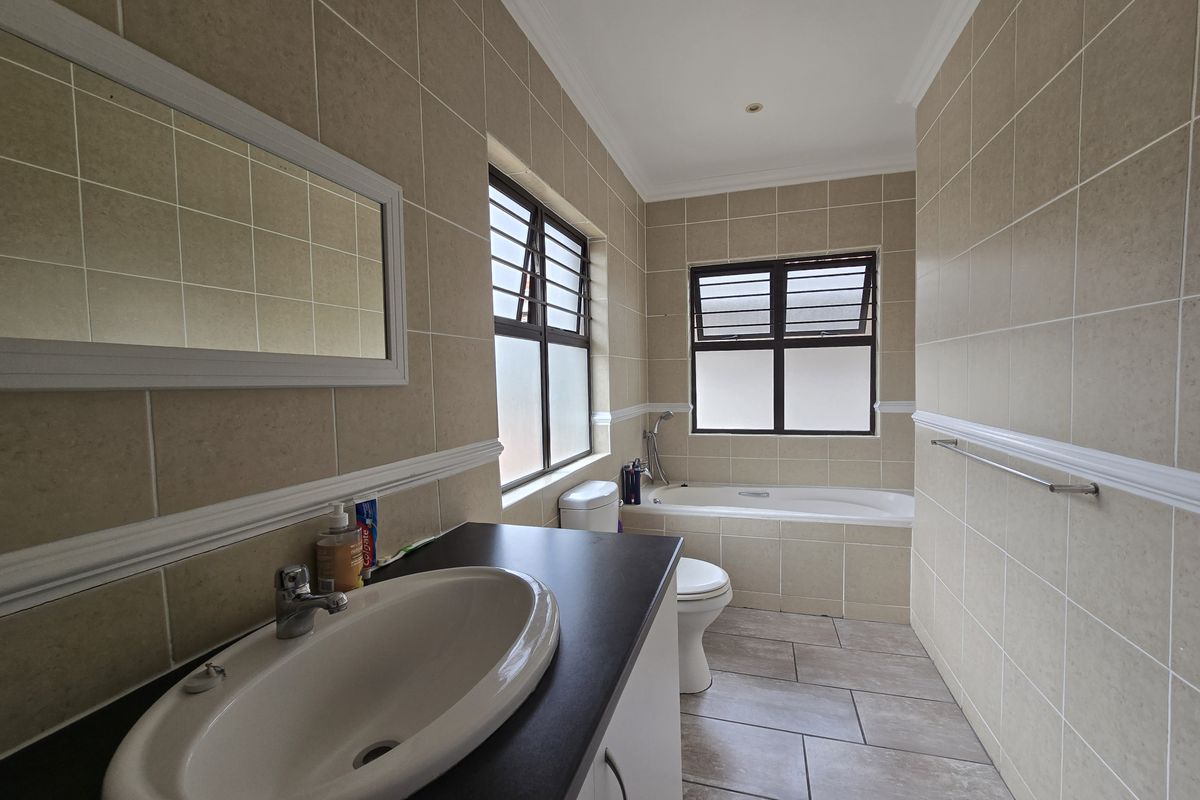 A well-maintained bathroom featuring a built-in vanity, tiled walls and flooring, a bathtub, and louver windows for natural ventilation.