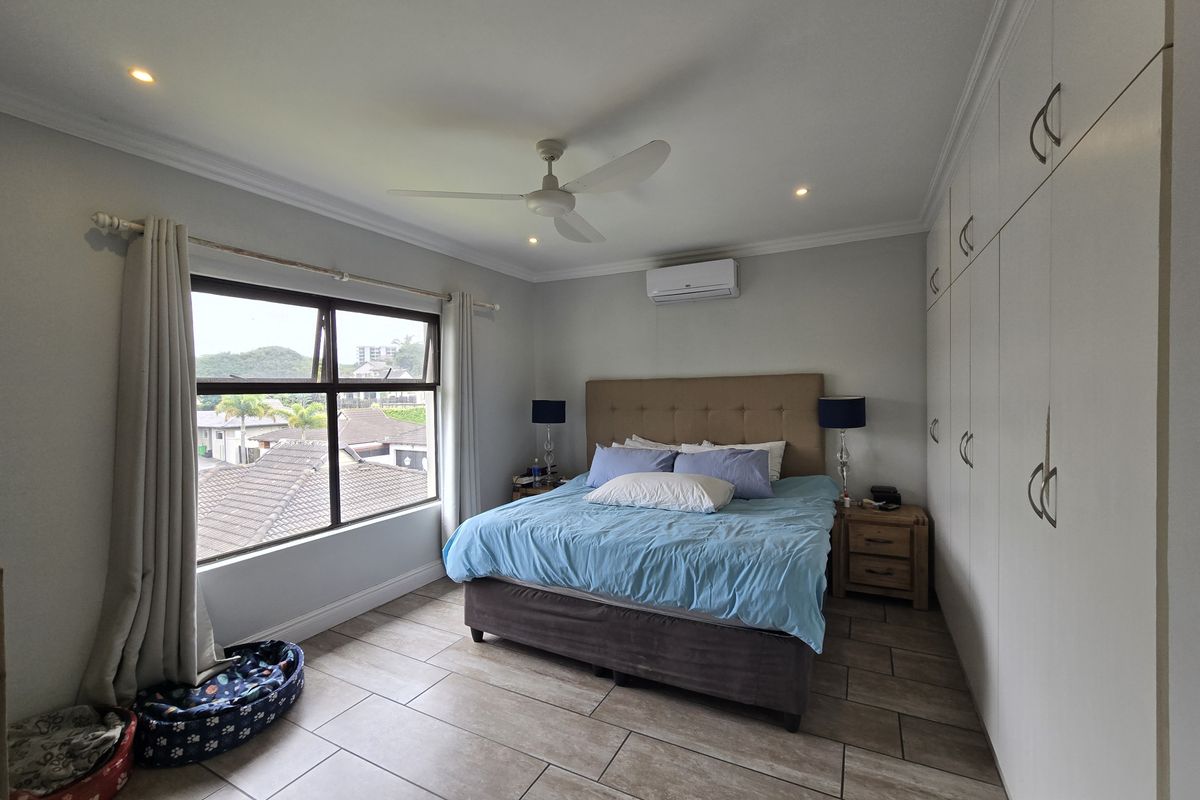 A well-maintained bedroom featuring tiled flooring, extensive built-in cupboards, a ceiling fan, and a split-system air conditioner for climate control.