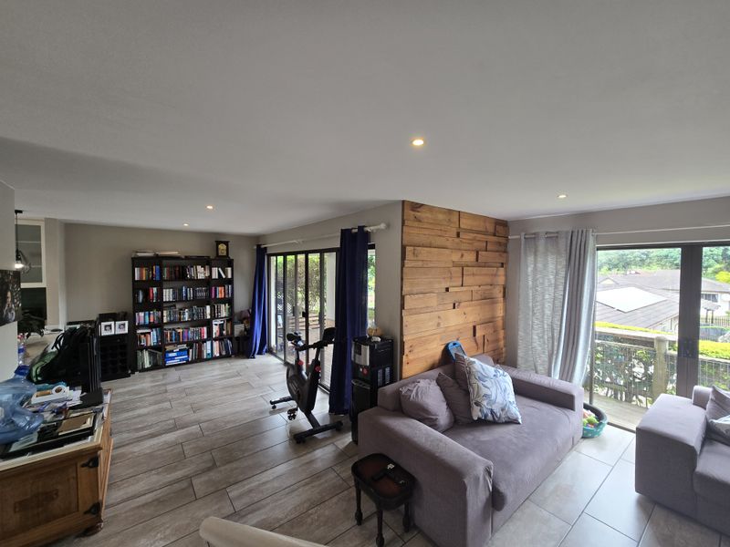 Spacious open-plan living area featuring modern tiled flooring, recessed downlights, and a distinctive timber feature wall with access to an outdoor balcony.
