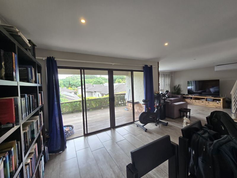 Spacious open-plan living area featuring tiled floors, recessed lighting, and large sliding doors opening onto a wooden deck with neighborhood views.